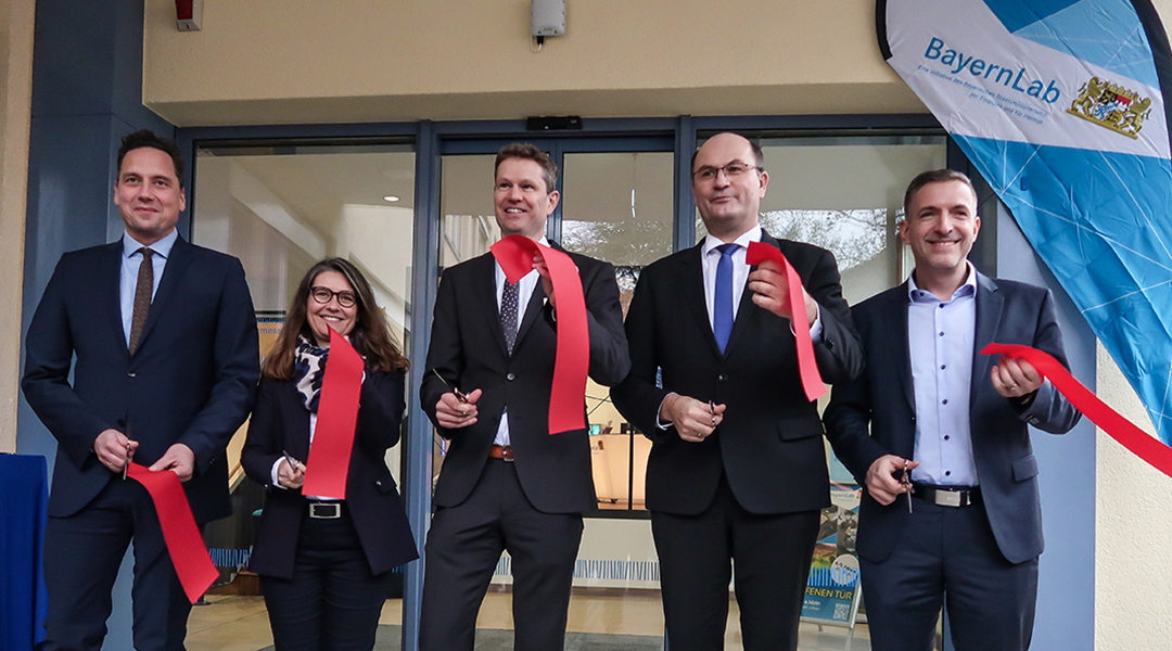 Eine Frau und vier Männer im Anzug stehen vor der Eingangstür des BayernLabs und halten ein Stück des durchtrennten roten Eröffnungsbandes in der Hand.
